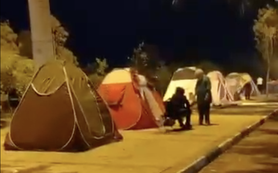 Night time picture of tents streetside with a few people alongside the tents.