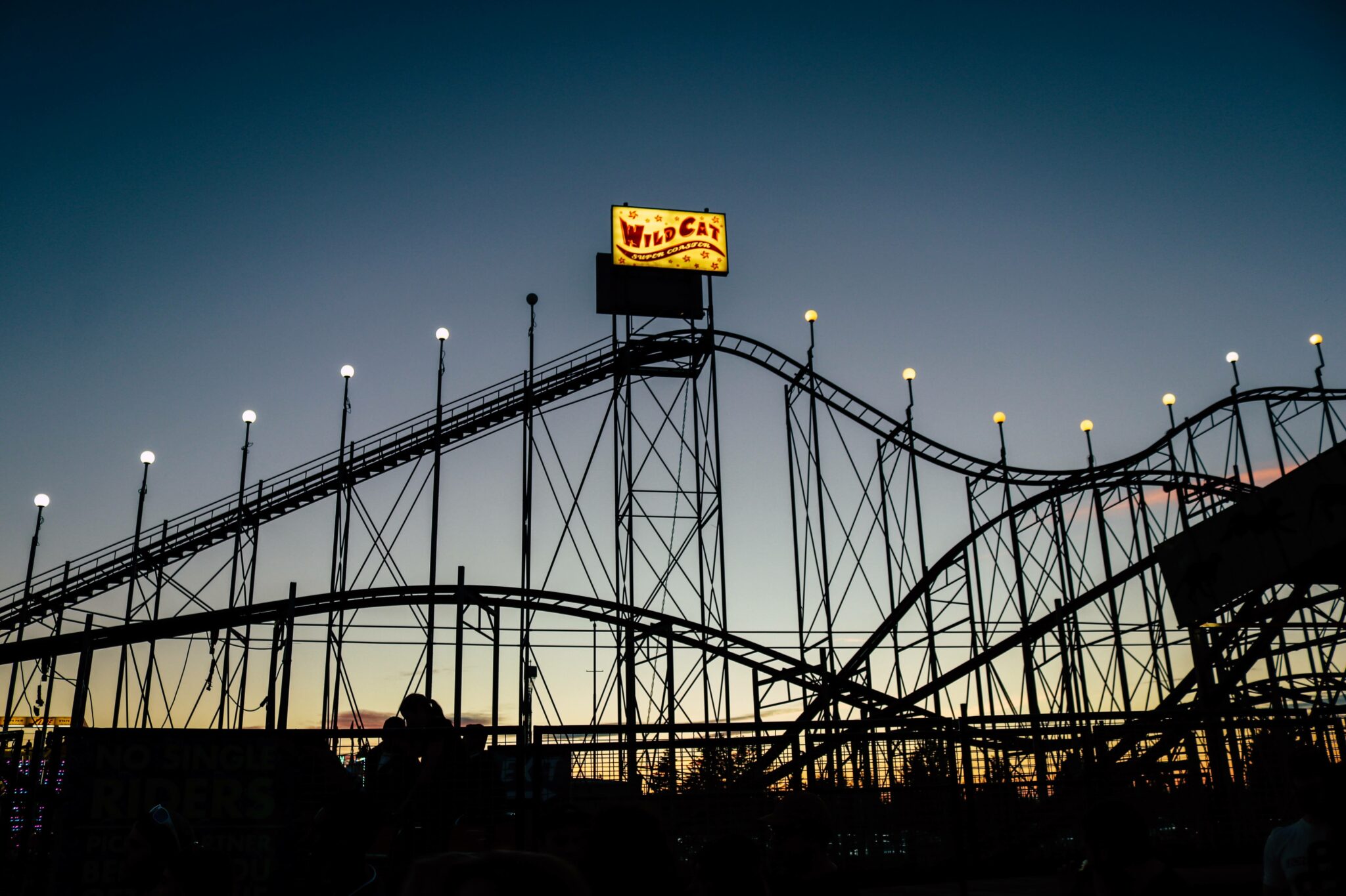 A sun sets behind a roller coaster, making the roller coaster a silhoutte
