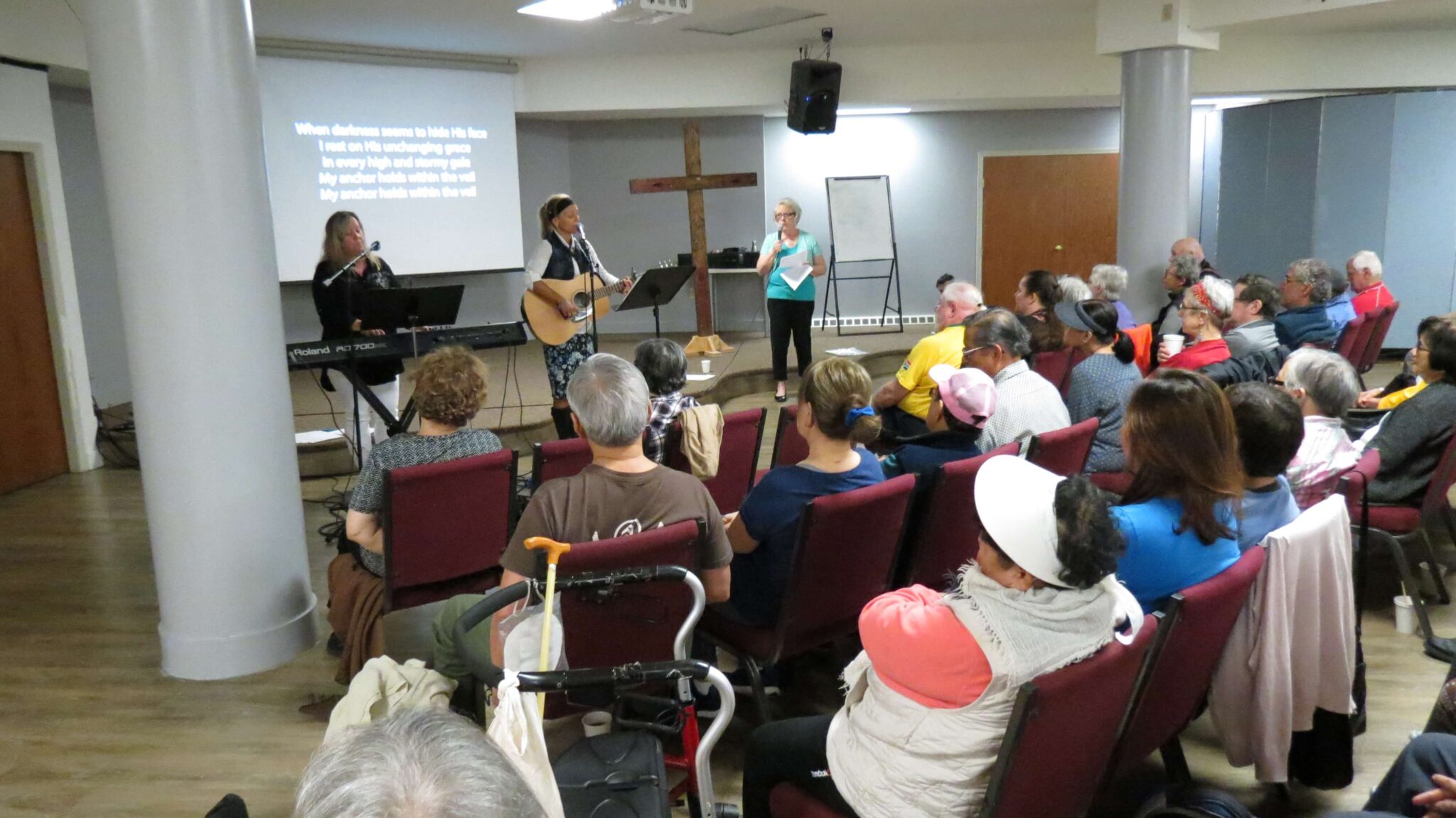 A group of people are sitting in chairs facing people leading worship.