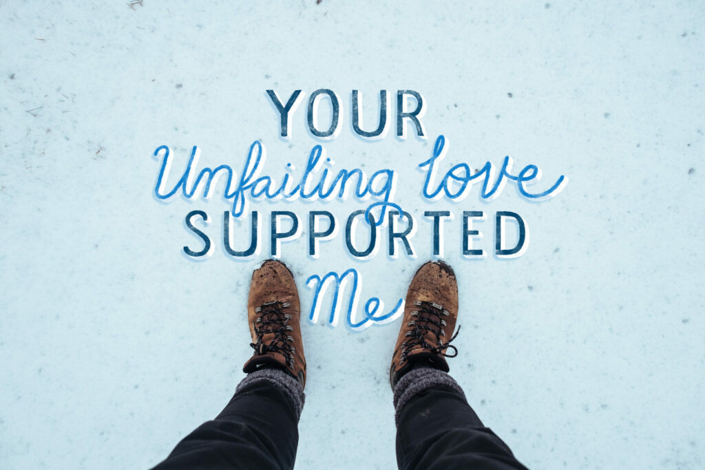 The camera is looking down at a person's feet and leggings as they stand in the snow. Hand lettering reads "Your unfailing love supported me."