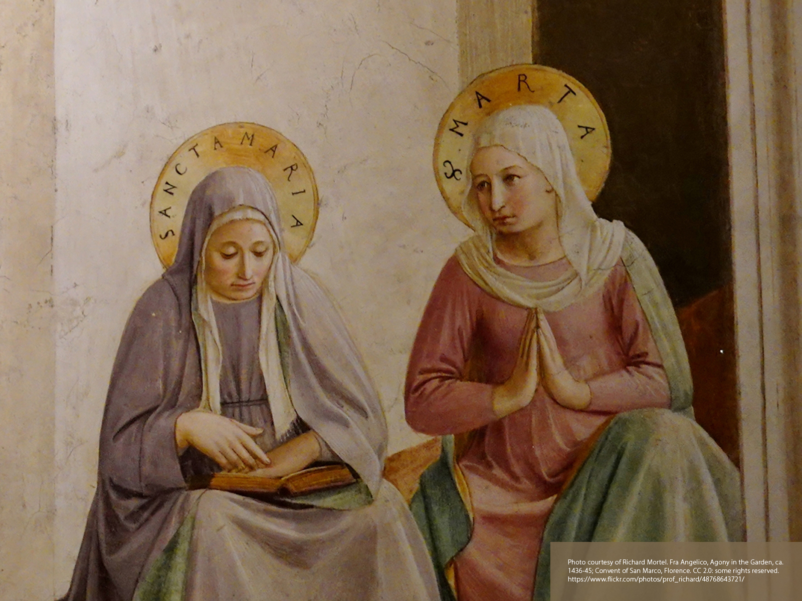 A medieval style painting of two people sitting beside each other. They both have halos, one is praying and one is holding a book