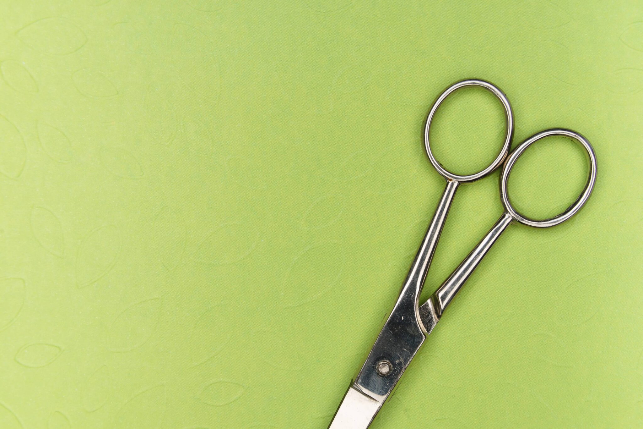 A pair of silver scissors with a green background.
