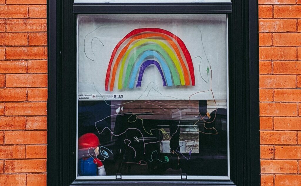 A rainbow is painted in the window of a brick building