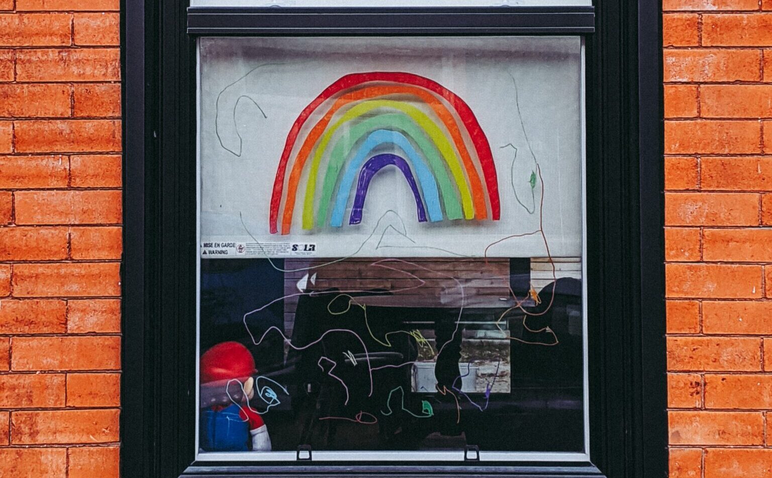 A rainbow is painted in the window of a brick building