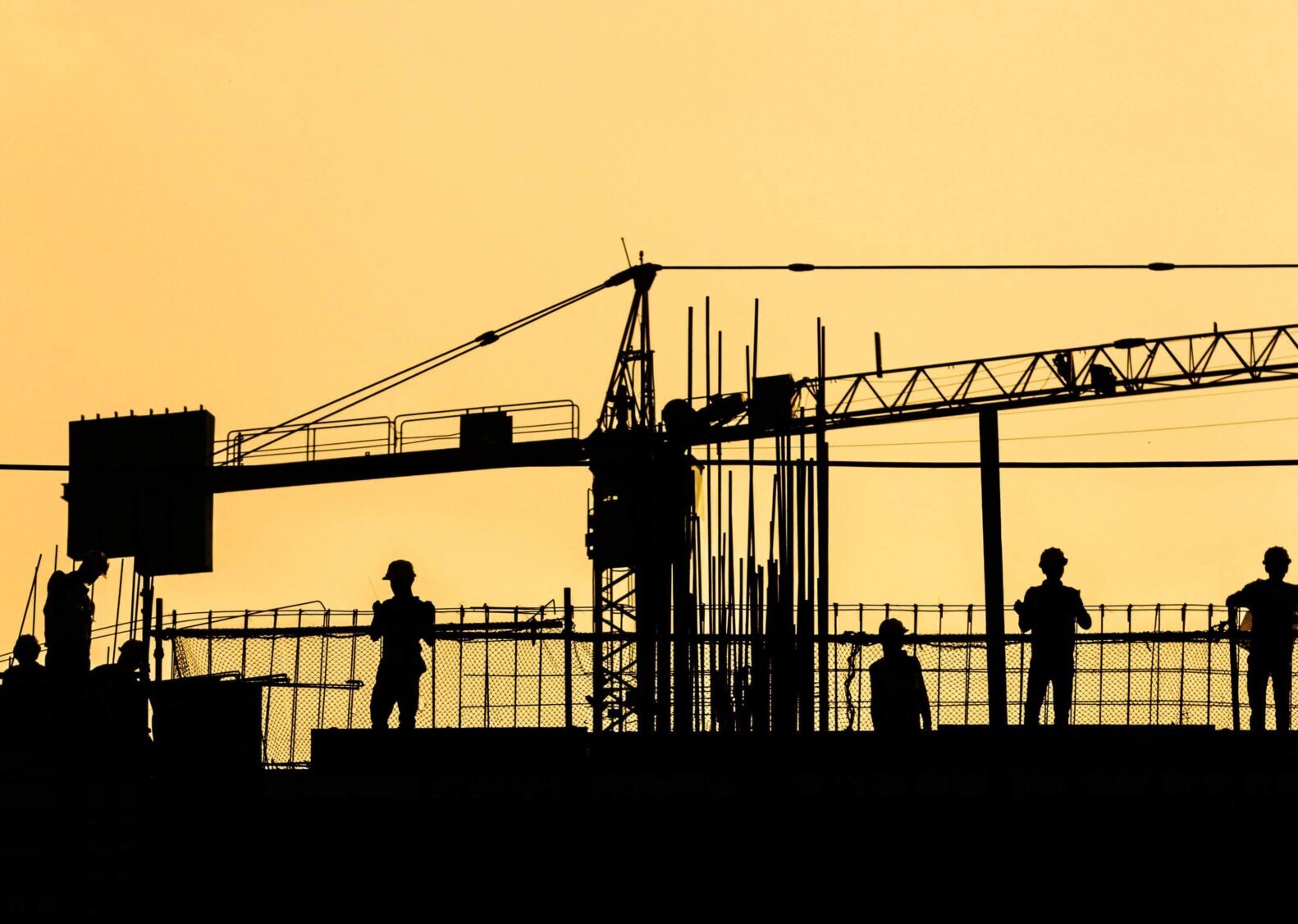 A silhouette of people at a construction site. There is a crane.
