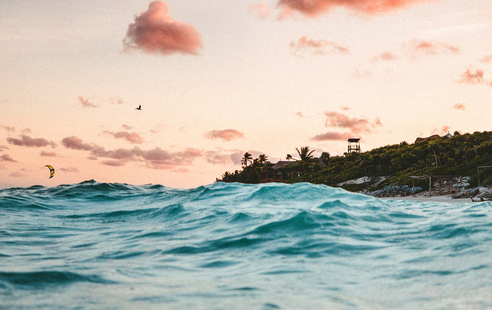 A sunset in the Caribbean. Waves in the foregroudn with the island rising from the sea.