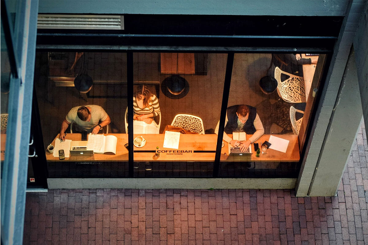 People are sitting at a table in a cafe. The photo is taken from outside the cafe through a window