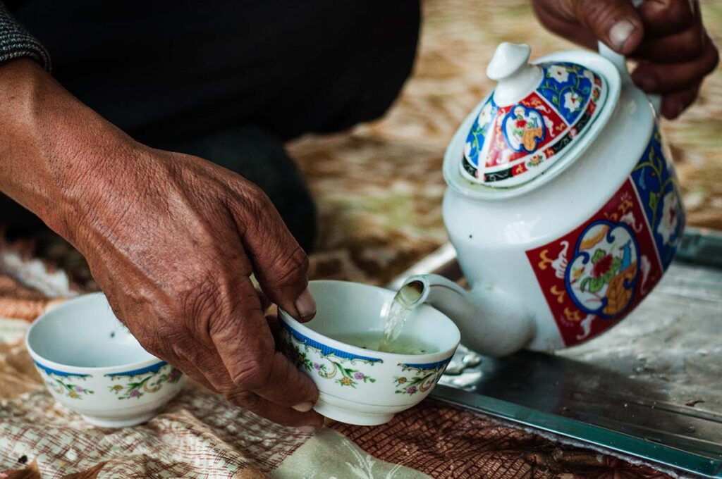 Image of a Tajik woman pouring a cup of tea from a colourful, ornate teapot.