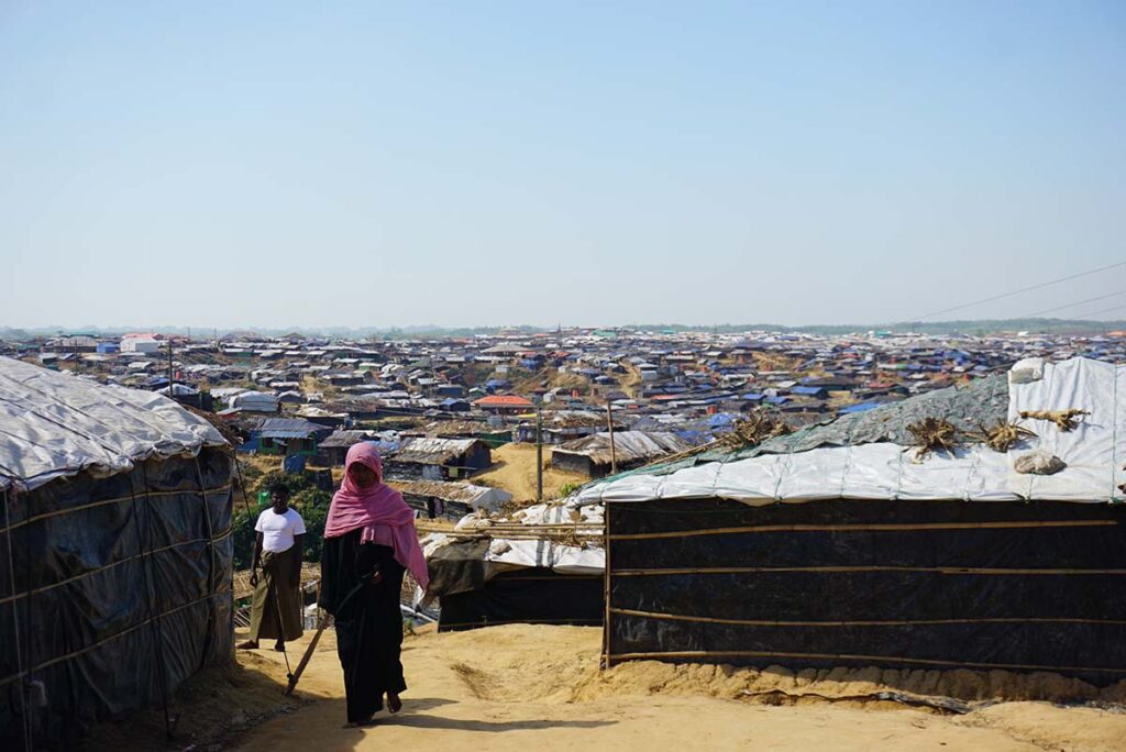 Two women walking on a dirt road inside a refugee camp.