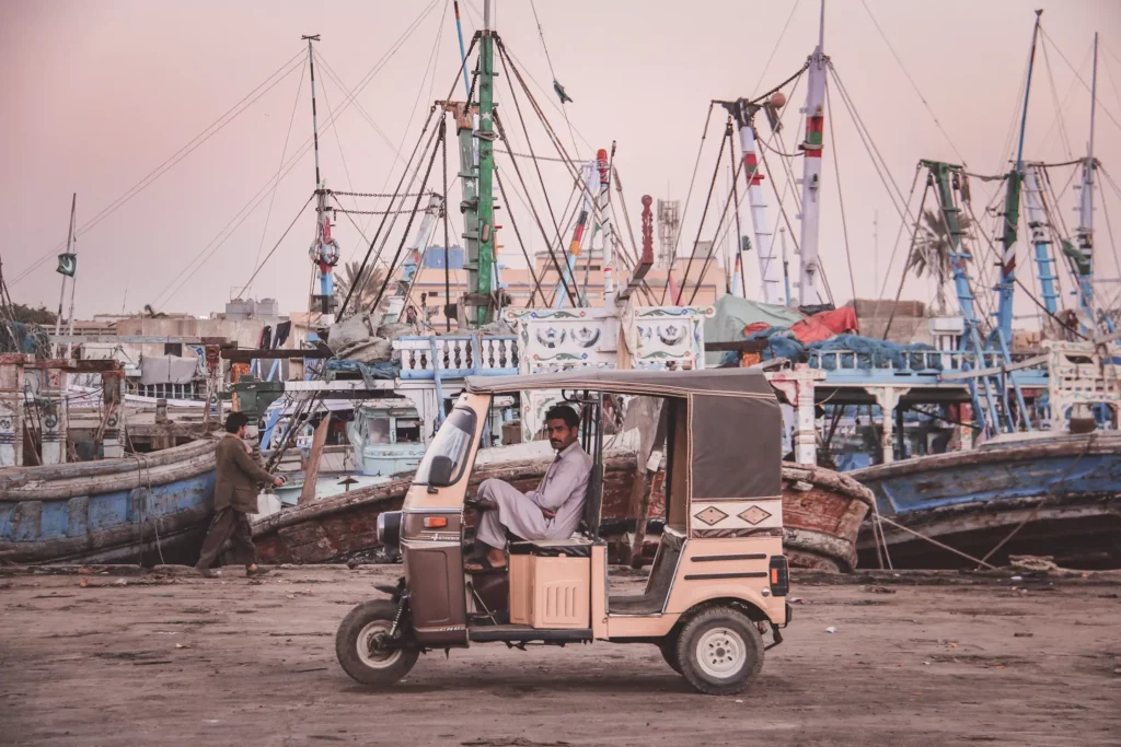 Man sitting in a tuk tuk in a busy port.